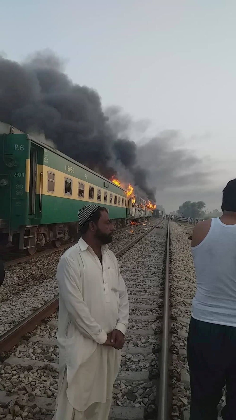 A man stands in front of a burning train after a gas canister passengers were using to cook breakfast exploded, near the town of Rahim Yar Khan  / JAWEDASRAR SIDDIQUI