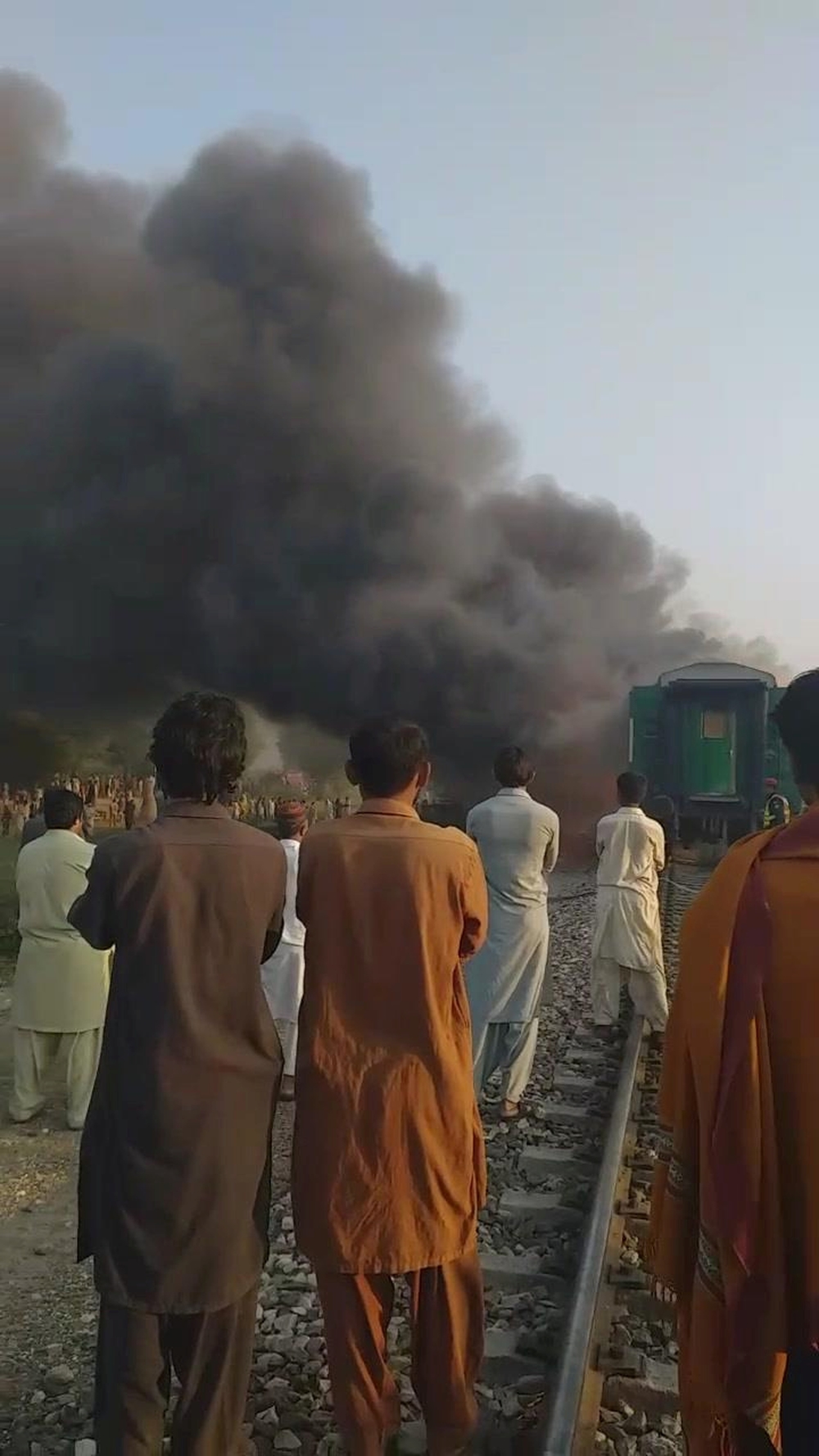 Men look at a burning train after a gas canister passengers were using to cook breakfast exploded, near the town of Rahim Yar Khan  / JAWEDASRAR SIDDIQUI